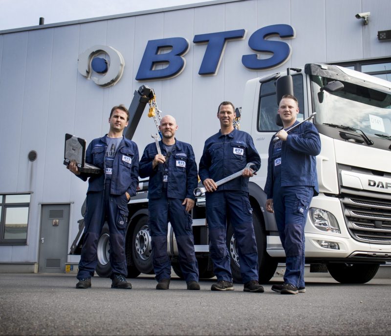 Die vier BTS Mechaniker, die sich für den DAF Service Cup 2019 qualifiziert haben, stehen nebeneinander vor einem DAF CF Lkw mit Absetzkipper Aufbau. Jede der Personen trägt blaue Arbeitskleidung einer Lkw Werkstatt und hält ein Werkzeug in den Händen.